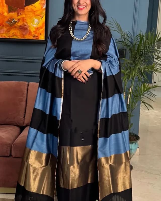 Woman wearing a black, blue, and gold outfit with a striped shawl indoors.